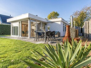 A modern house with a covered patio, a dining area with chairs, and a large planter. - Holiday Home in Renesse With Swimming Pool (Renesse)