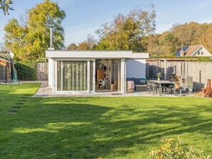 A modern house with a glass door leading to a patio area, a small garden, and a wooden fence. - Holiday Home in Renesse With Swimming Pool (Renesse)