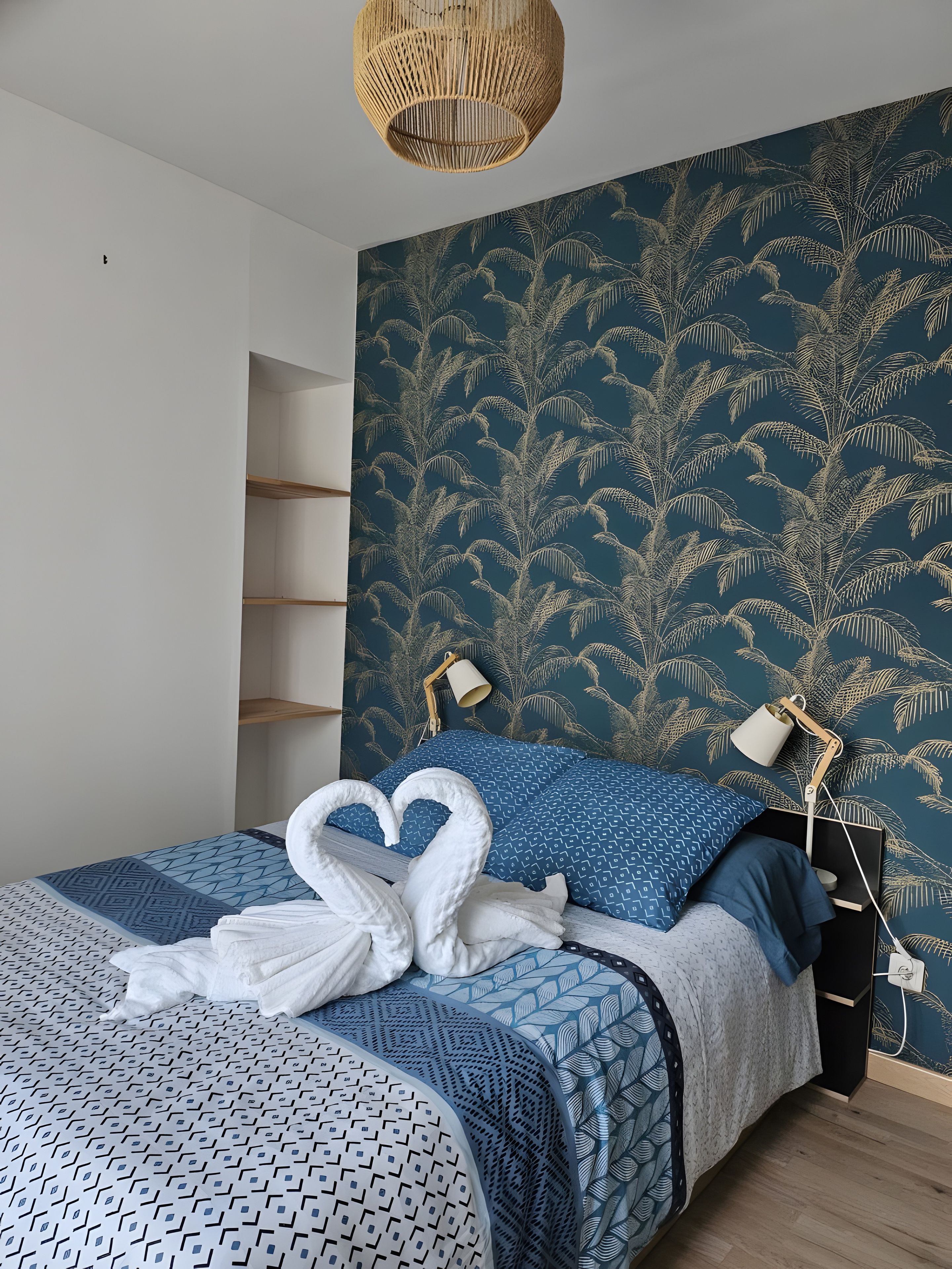 A bedroom with a bed, two bedside lamps, a wall-mounted shelf, and a decorative wall with a leaf pattern.