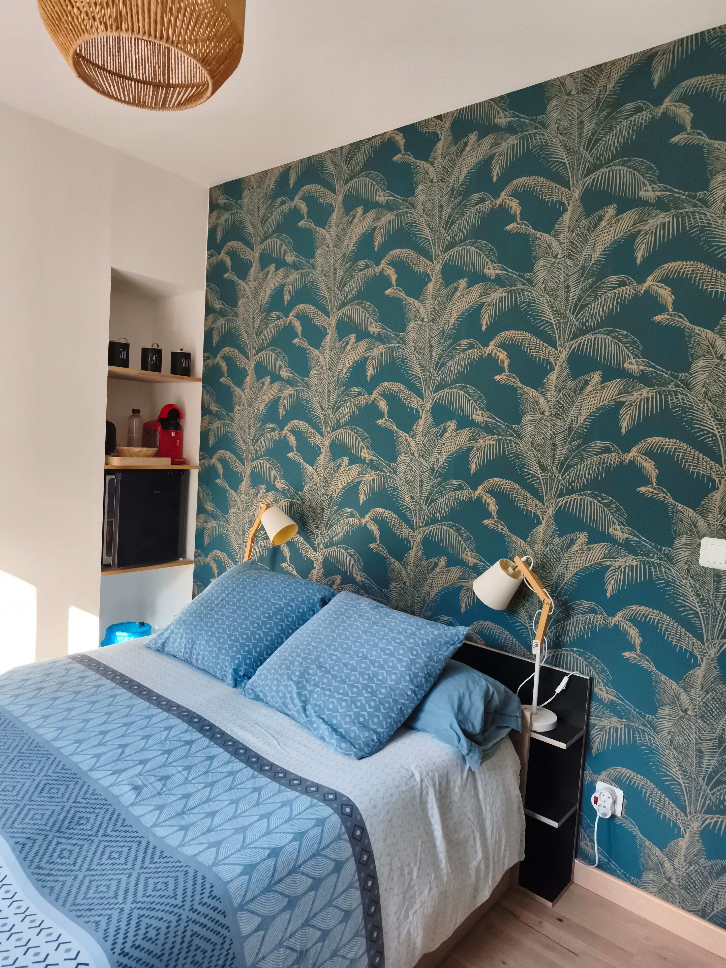 Ein Schlafzimmer mit einem Bett, zwei Nachttischlampen, einem Regal mit Gegenständen und einer Wand mit einem blättrigen Muster.