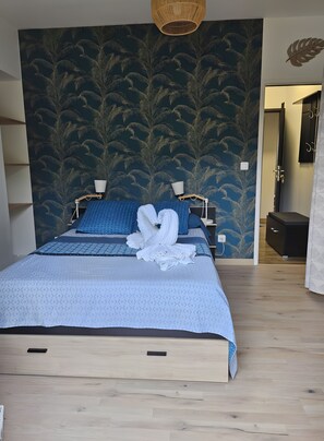 A bedroom with a bed, a wooden floor, a wall with a leaf pattern, and a door. - Bed and Breakfast 'Agréables Chambres D'hôtes -' with Wi-Fi (Guécélard)