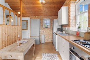 A kitchen with wooden beams, a brick wall, a window, and a dining area with a table and chairs. - The Barn A Cosy Countryside Retreat Near Eastbourne (Eastbourne)