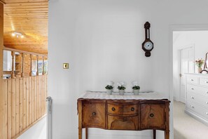 Eine Holztreppe führt zu einem Raum mit einer hölzernen Kommode, einer an der Wand befestigten Uhr und einer weißen Tür.