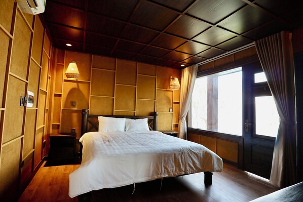 Habitación de hotel con techo de madera, cama con ropa de cama blanca, dos lámparas de noche, mesita de noche y ventana con cortinas.