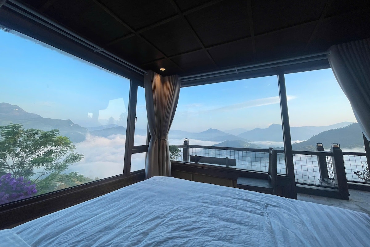Una habitación con una cama, ventanas amplias y vistas a montañas.