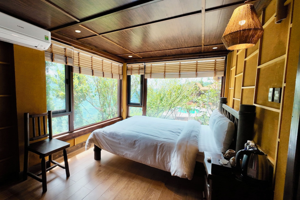 Un dormitorio con cama, una silla, un equipo de aire acondicionado y vistas a la vegetación exterior.