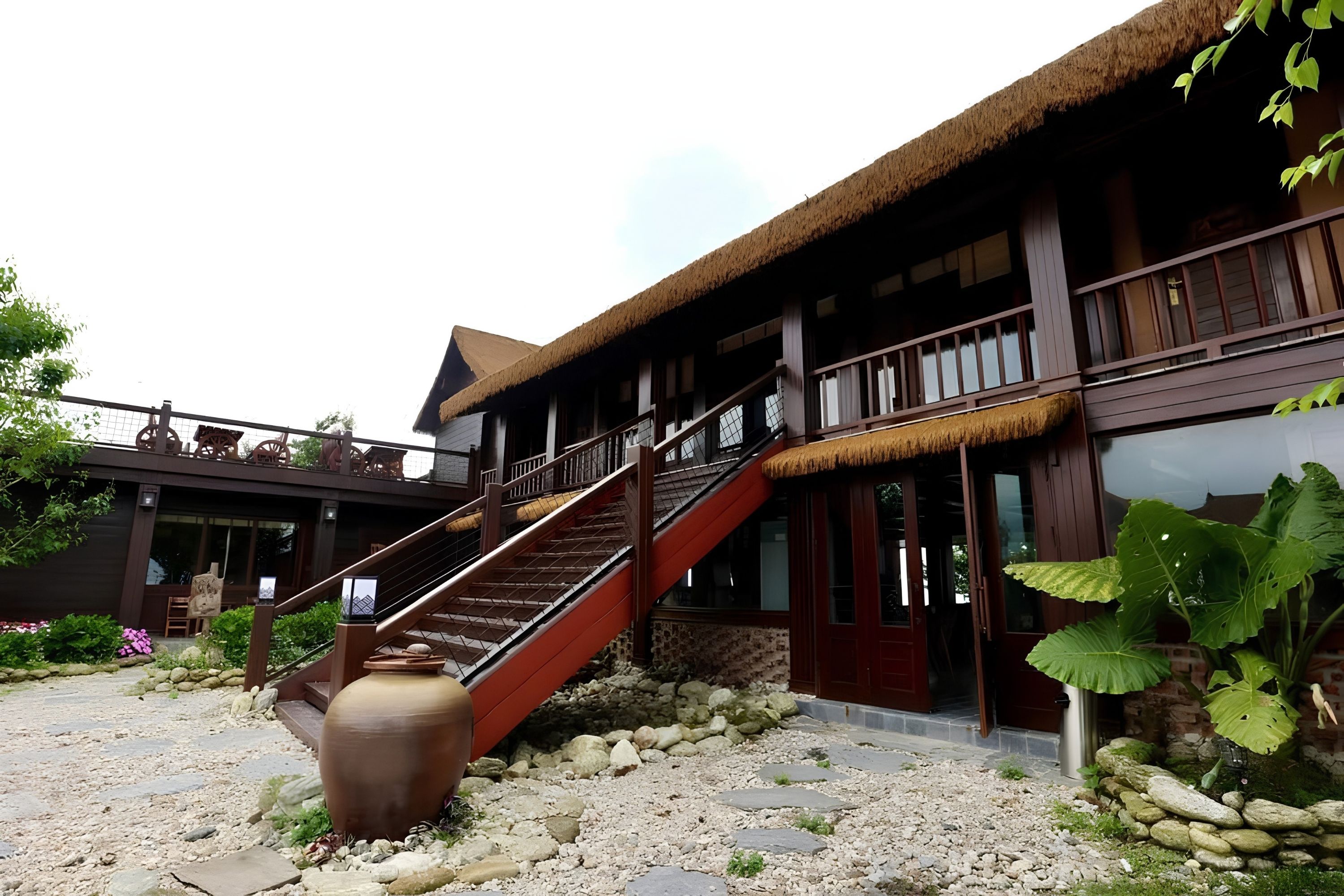 A traditional building with a staircase leading to a second floor, surrounded by a garden with rocks and plants.