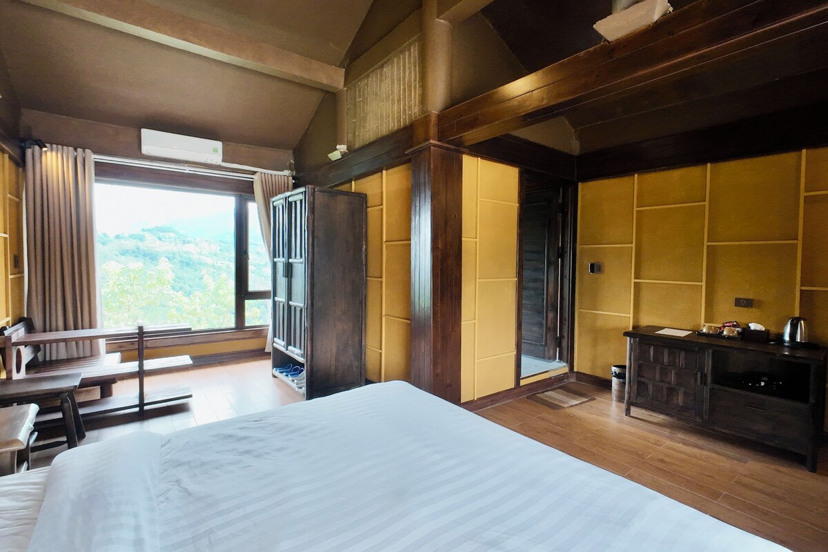 A hotel room with a large bed, wooden furniture, a desk, and a view of the outdoors.