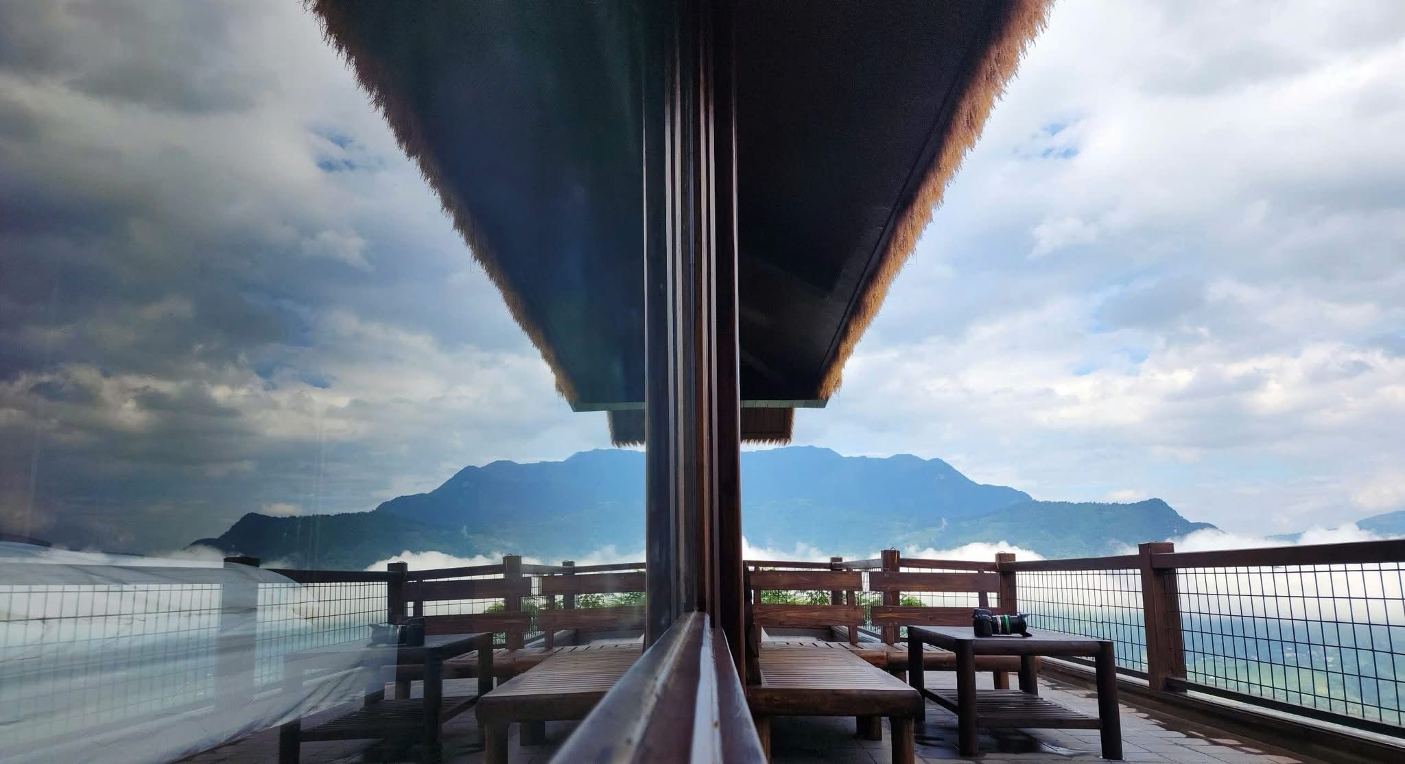 A balcony with wooden benches and a glass railing overlooking a mountainous landscape.
