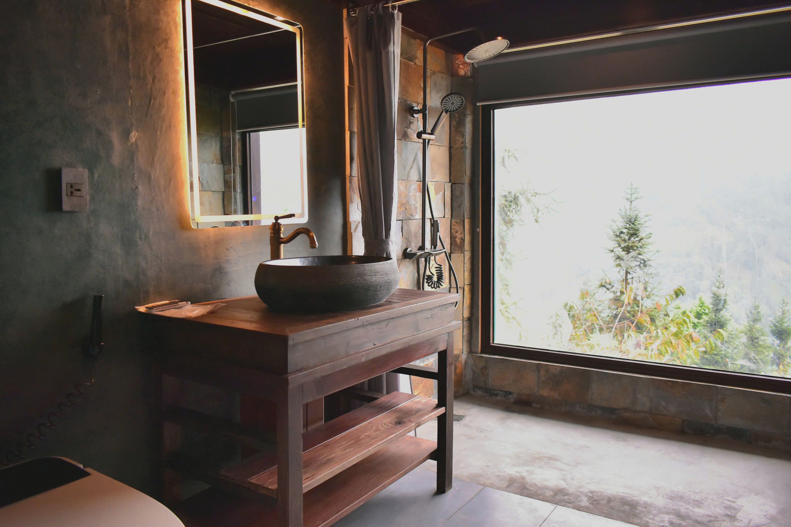 A rustic bathroom with a large window, a wooden vanity, and a stone wall.