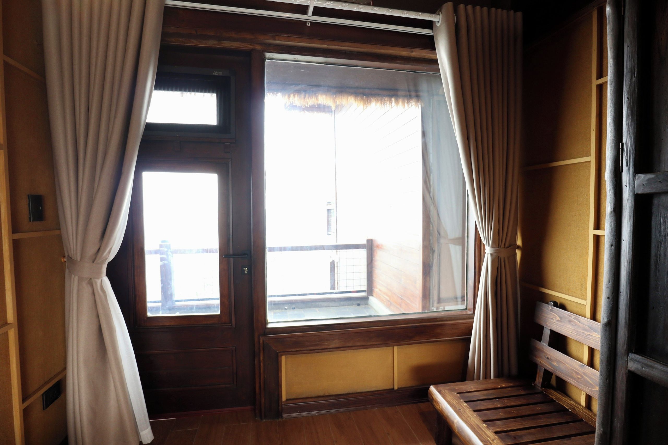Una habitación con un banco de madera, una ventana con cortinas y vistas al exterior.