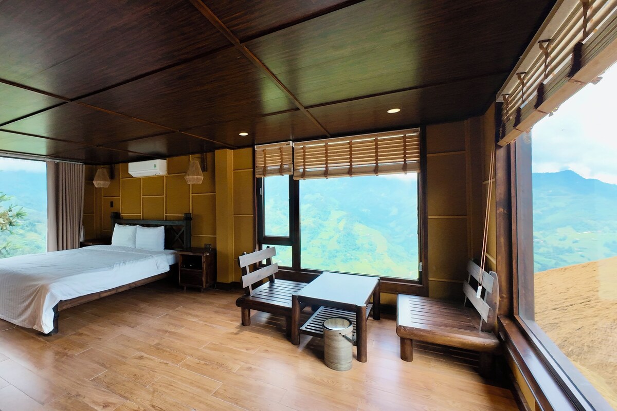 A bedroom with a large bed, a wooden desk, and a view of the mountains.