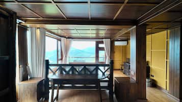 A wooden interior with a table and chairs, a window with curtains, and a view of mountains.