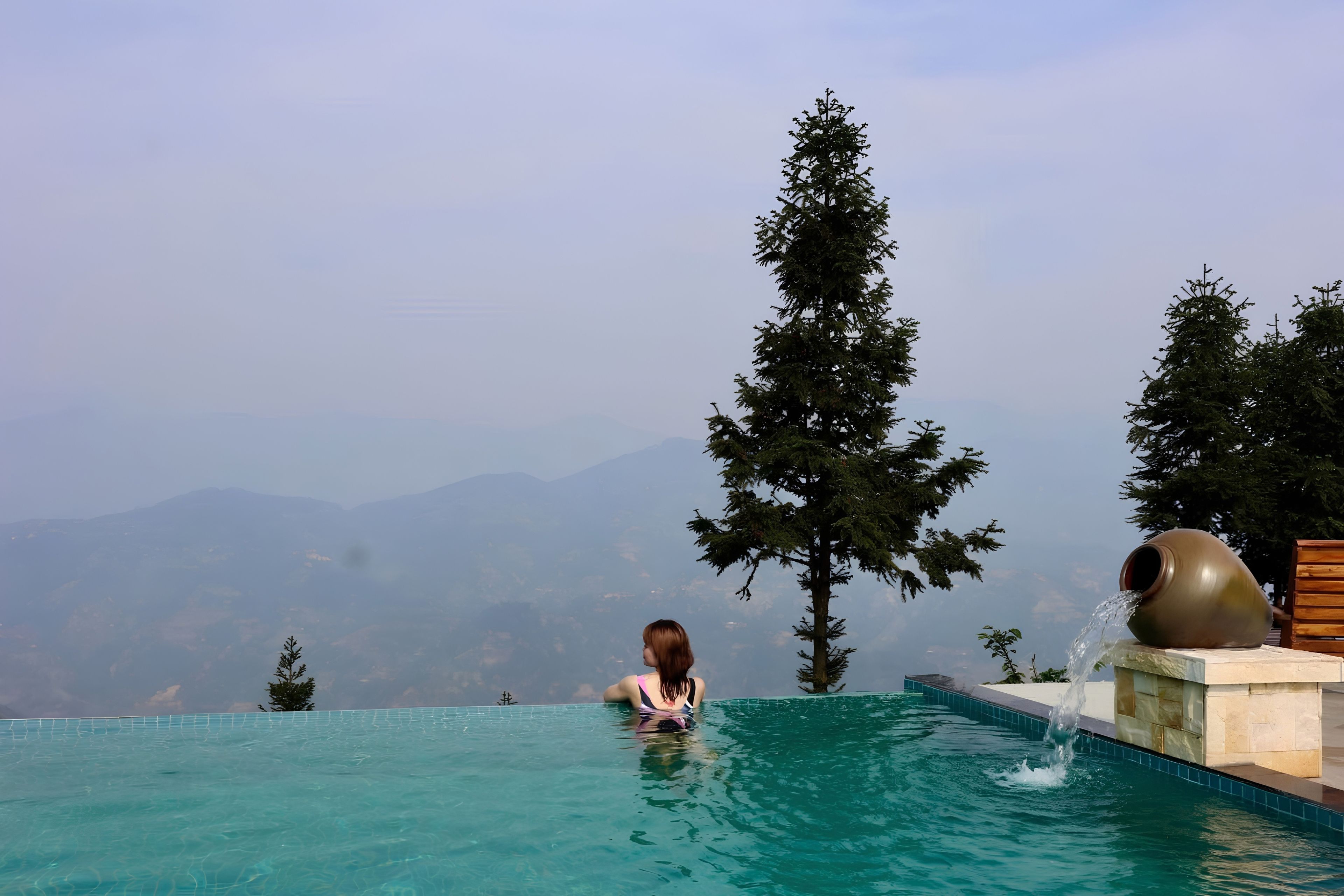 Una persona en una piscina infinita azul cristalina con vistas a montañas lejanas.