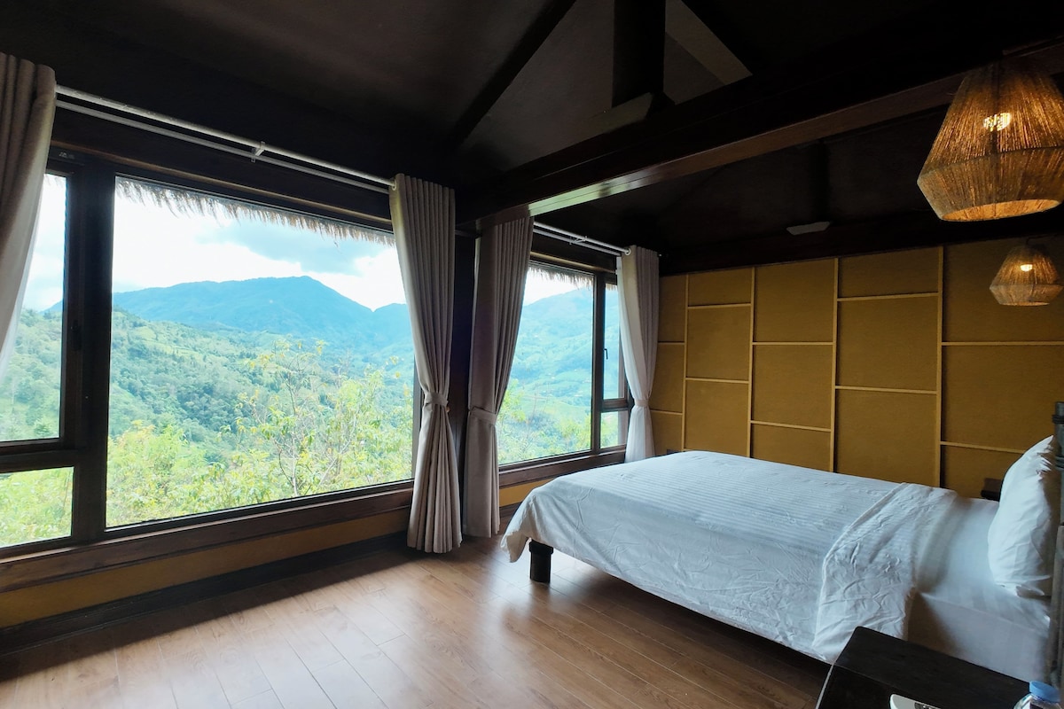 Un dormitorio con un ventanal grande, suelo de madera y una cama.