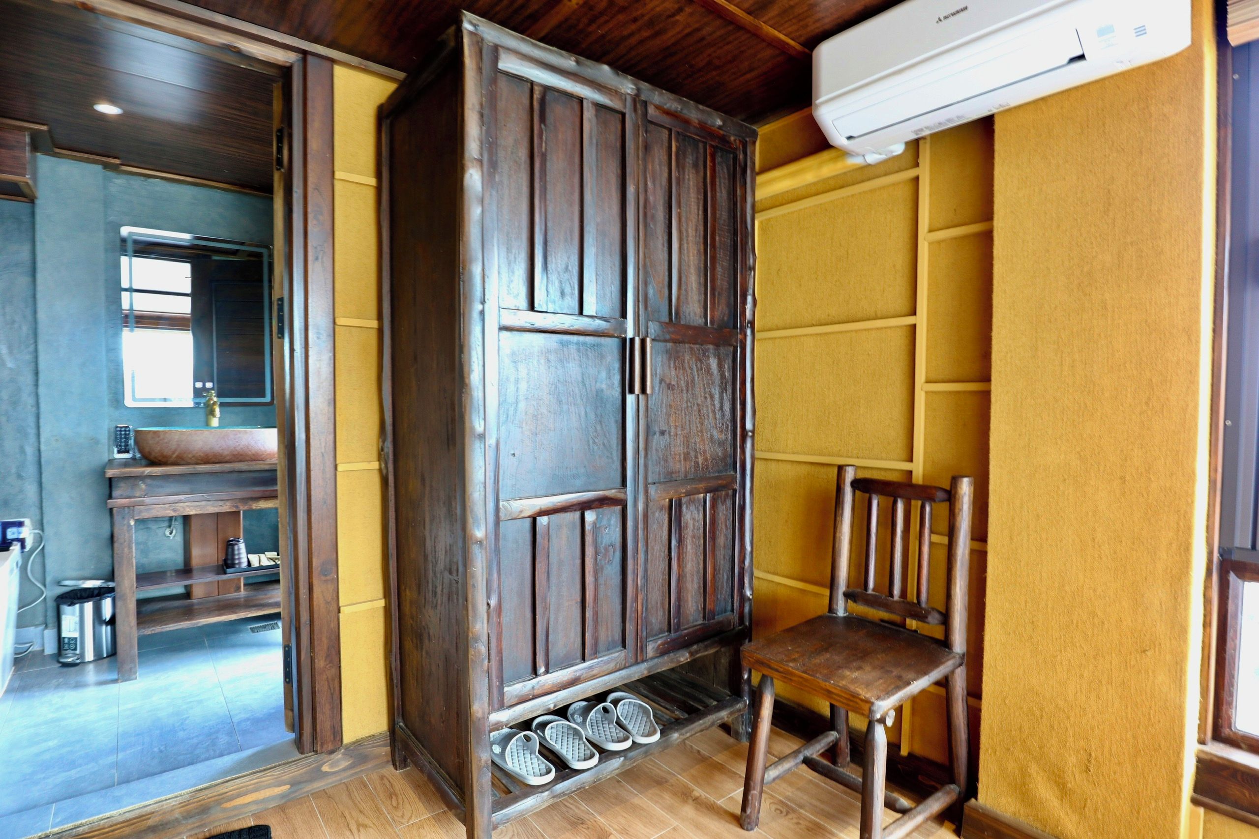 A room with a wooden wardrobe, a chair, and a sink.
