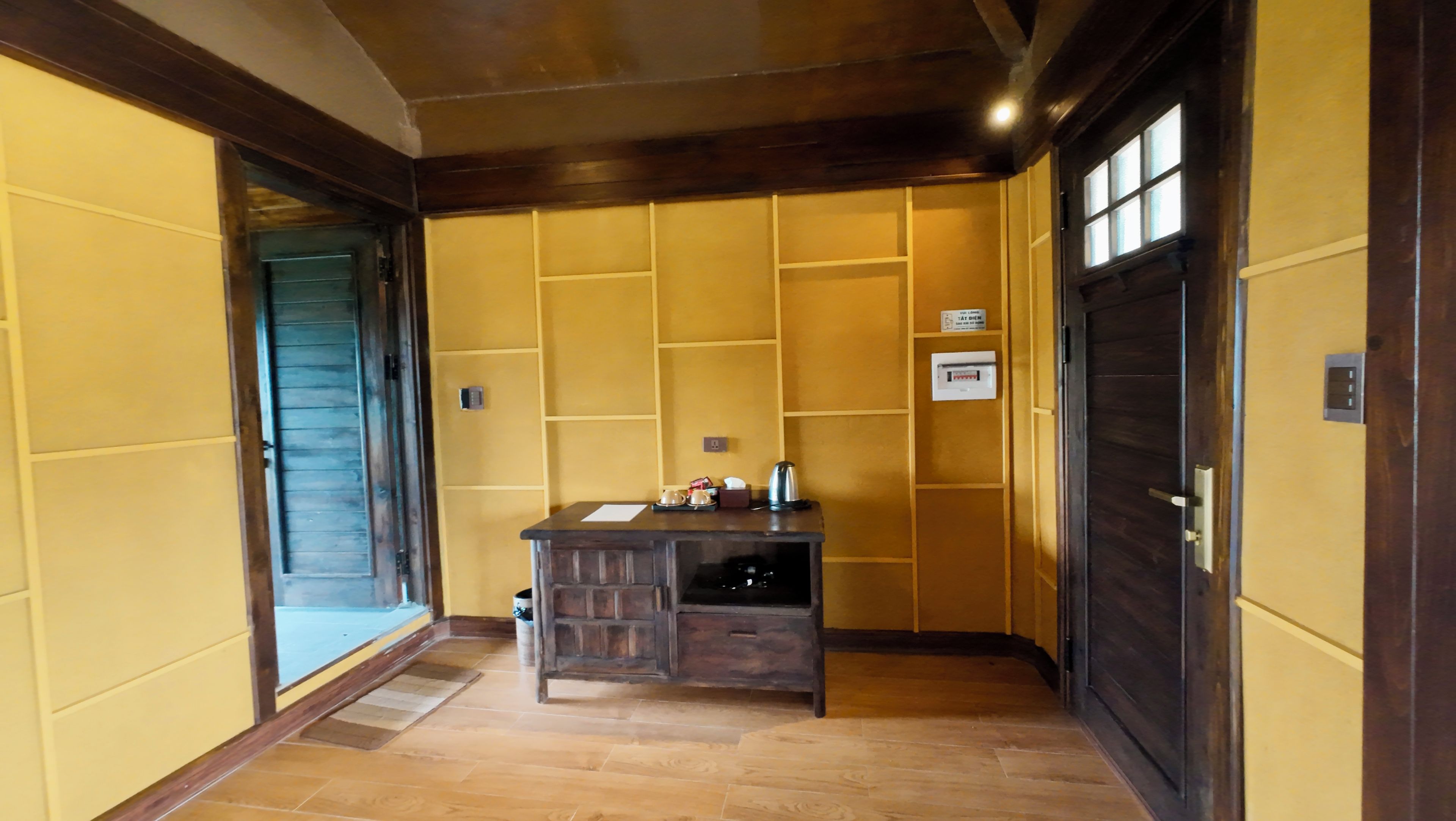 A hallway with yellow walls, a wooden desk with a kettle, and a door with a window.