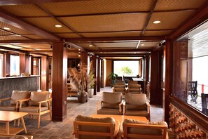 A spacious indoor area with wooden flooring, multiple seating arrangements including sofas and chairs, and a large window providing a view outside. - Ban Luoc Ecolodge (Hoang Su Phi)