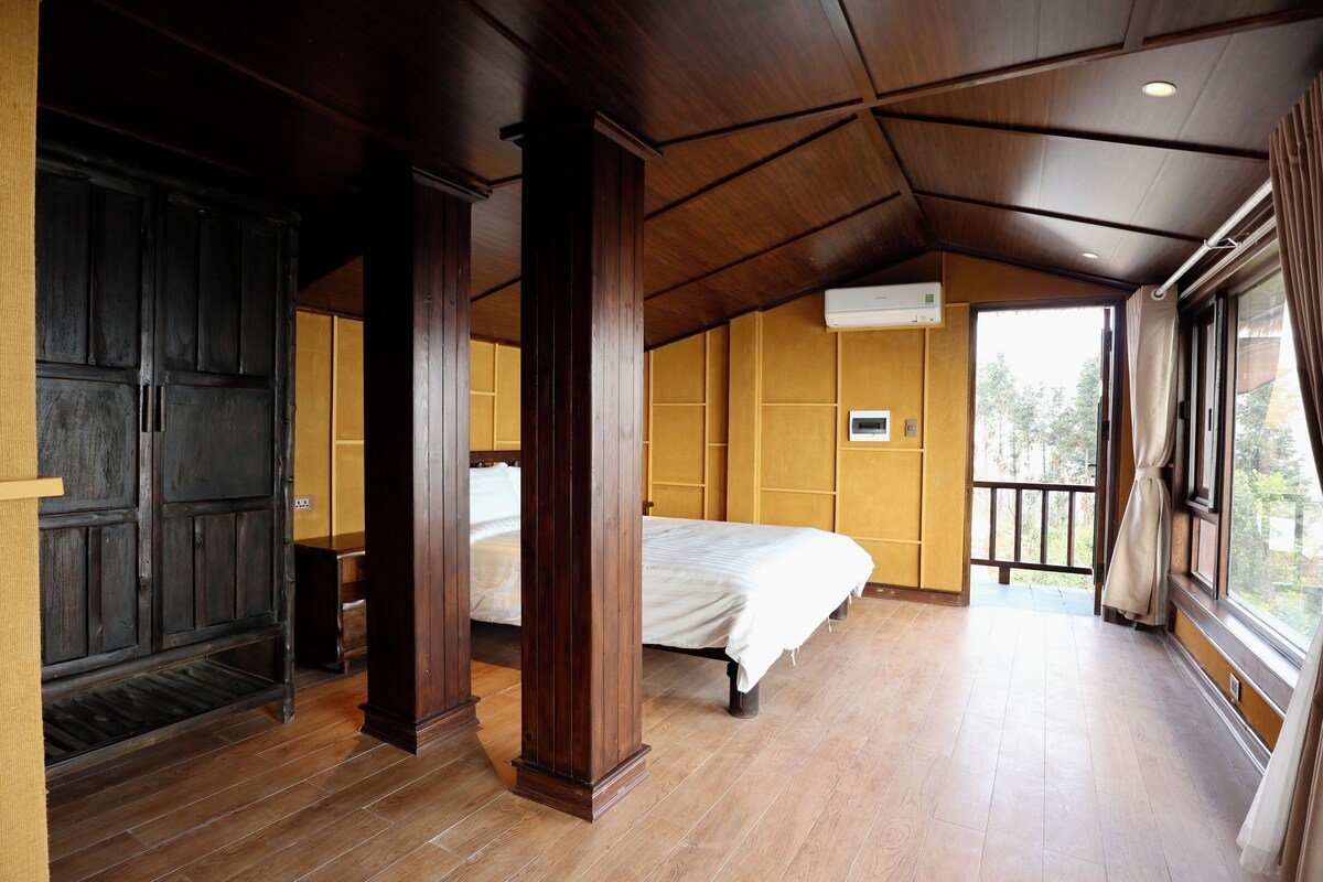 A room with wooden flooring, a bed, a wardrobe, and a window with curtains.