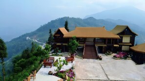 A traditional wooden house with a thatched roof, a stone staircase, and a view of a mountain valley. - Ban Luoc Ecolodge (Hoang Su Phi)