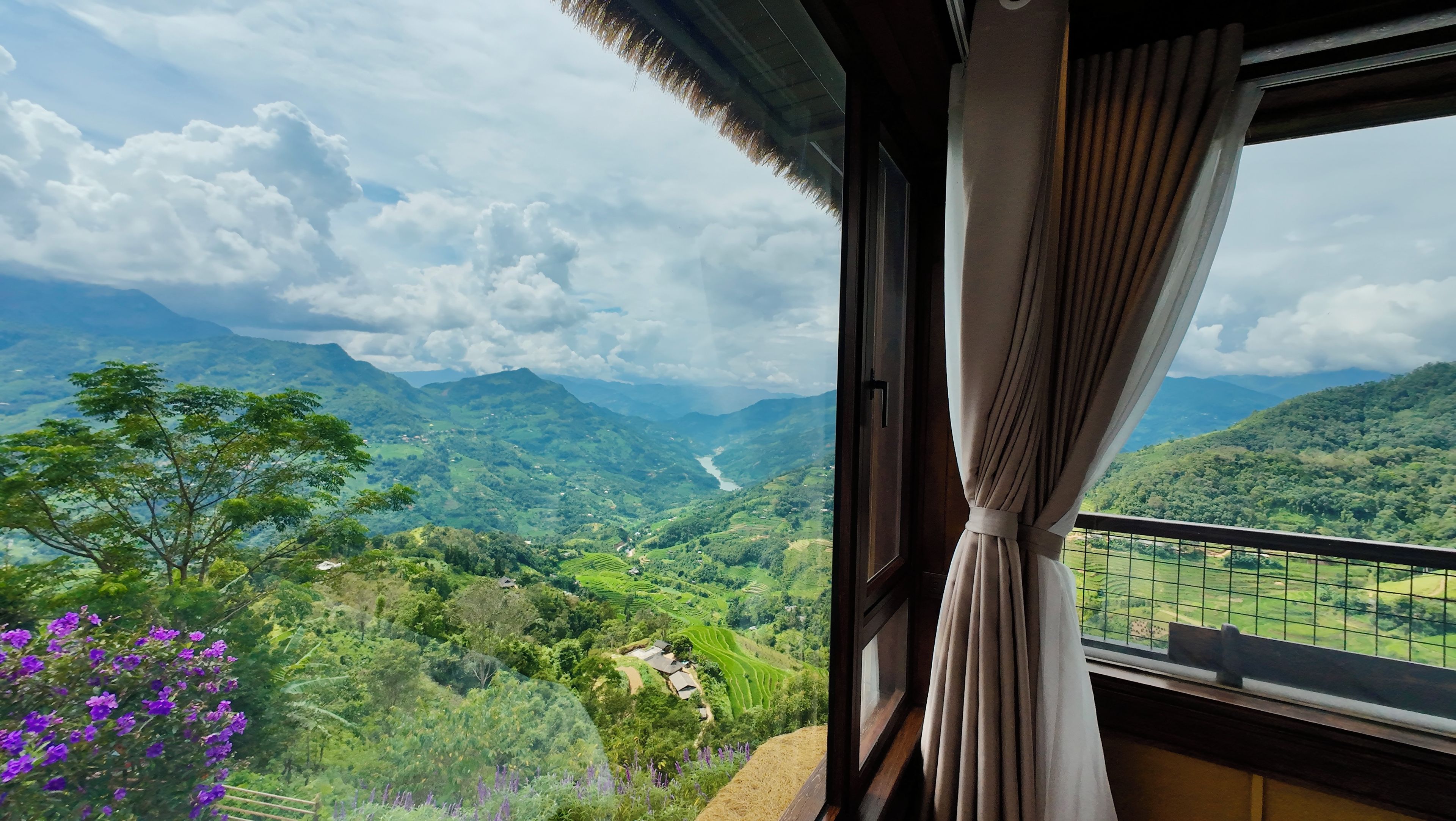 A room with a view of a mountainous landscape through a window with curtains.