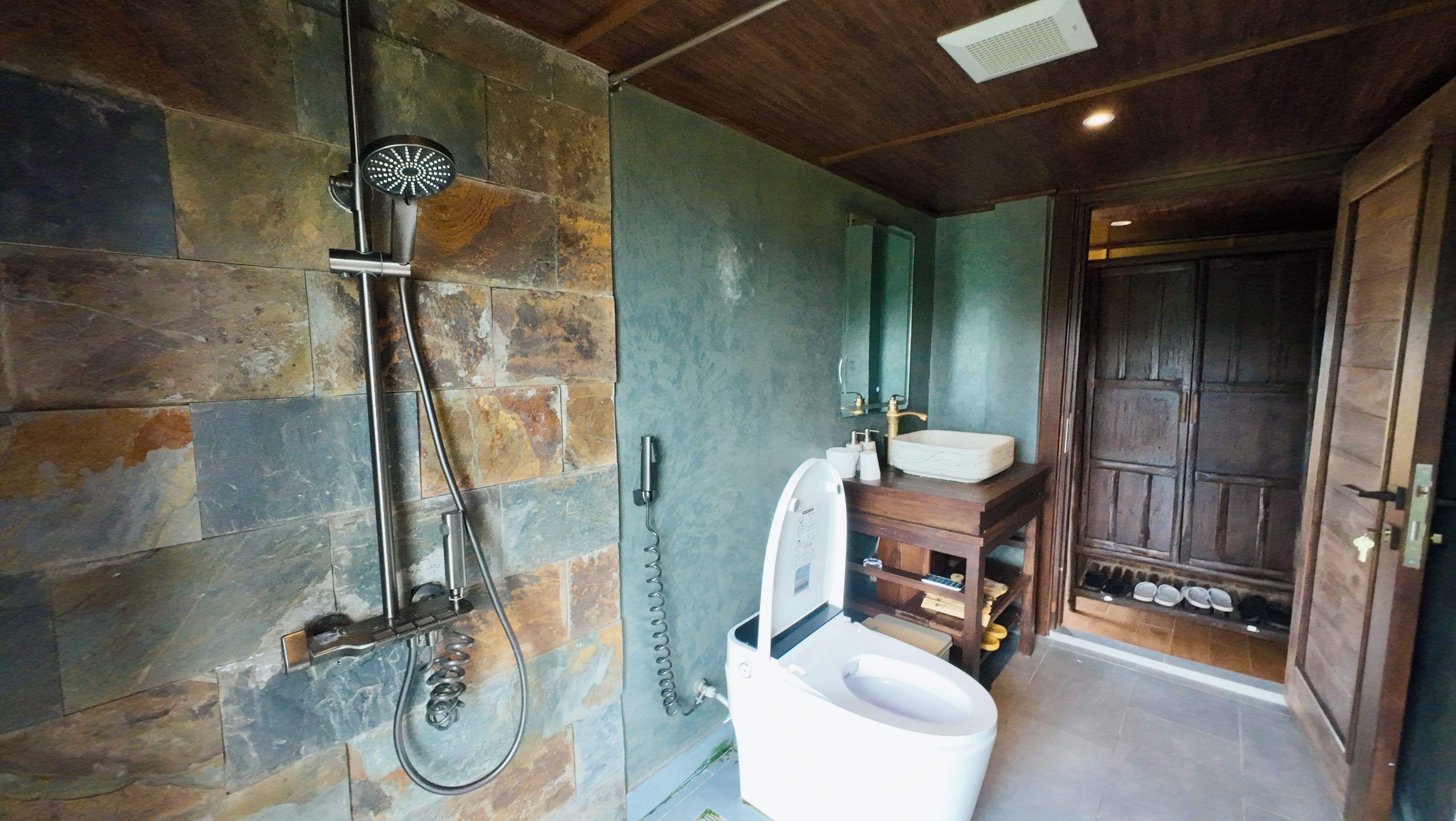 Un baño con pared de piedra, ducha, lavabo y puerta de madera.