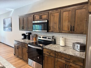 A modern kitchen with wooden cabinets, stainless steel appliances, and a granite countertop. - Luxury Gull Lake Getaway 5BR • 5BA • Private Boat Slip (Nisswa)