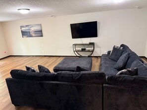 A living room with a sectional sofa, a flat-screen TV mounted on the wall, and a wooden floor. - Luxury Gull Lake Getaway 5BR • 5BA • Private Boat Slip (Nisswa)