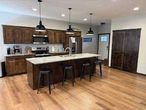 A modern kitchen with wooden cabinets, stainless steel appliances, a granite countertop, and bar stools. - Luxury Gull Lake Getaway 5BR • 5BA • Private Boat Slip (Nisswa)