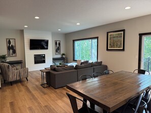 A modern living room with a large sofa, a dining table, and a flat-screen TV mounted on the wall. - Luxury Gull Lake Getaway 5BR • 5BA • Private Boat Slip (Nisswa)
