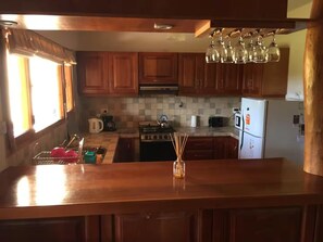 A kitchen with wooden cabinets, a stove, a refrigerator, and a window with curtains. - Casa con Excelente Vista en Bariloche máximo 8 pax (San Carlos de Bariloche)
