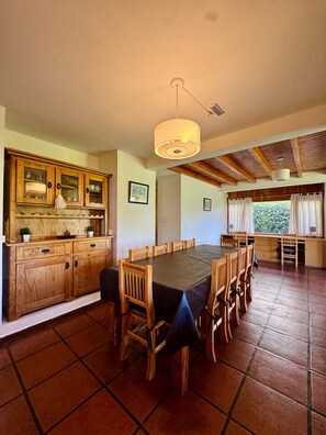 Uma sala de jantar espaçosa, com uma mesa comprida e cadeiras, armários de madeira e um lustre.