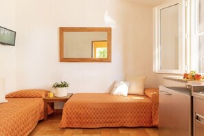 A compact room with two beds, a small table with a potted plant, a mirror, and a window with a view. - Argentario Giannutri: Superior Two-Bedroom Apartment, Sleeps 4 (Orbetello)