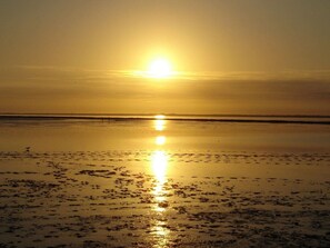 Ein Strand bei Sonnenuntergang mit ruhiger See und blauem Himmel.