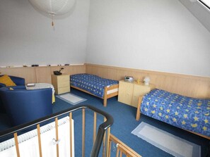 Ein Zimmer mit zwei Einzelbetten, einem Schreibtisch, einem Stuhl und einer kleinen Sitzecke.