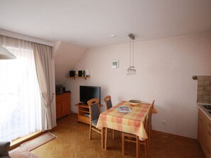 Ein gemütlicher Raum mit Esstisch, Stühlen, Fernseher und einer kleinen Küchenzeile.