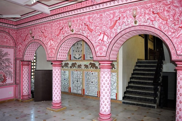 Una habitación con paredes de diseño rosa y blanco, una escalera y columnas.