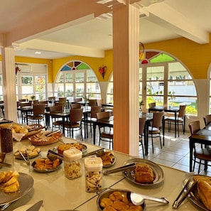 A restaurant with multiple tables and chairs, a variety of food items on display, and large windows allowing natural light. - Hotel Recanto dos Passaros de Sao Sebastiao (São Sebastião)