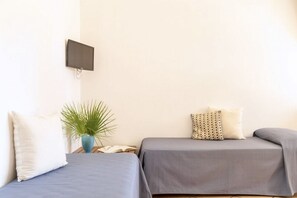 Ein Zimmer mit zwei Betten, einem an der Wand befestigten Fernseher, einer Pflanze und einem kleinen Tisch mit einem Buch.