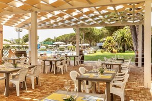 Un espace extérieur aménagé pour les repas, avec des tables et des chaises, une pergola et une vue sur une piscine et un espace verdoyant.