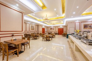 Un vaste espace dédié à la salle à manger, avec de nombreuses tables et chaises, un buffet équipé du matériel nécessaire au service des repas, et un lustre.