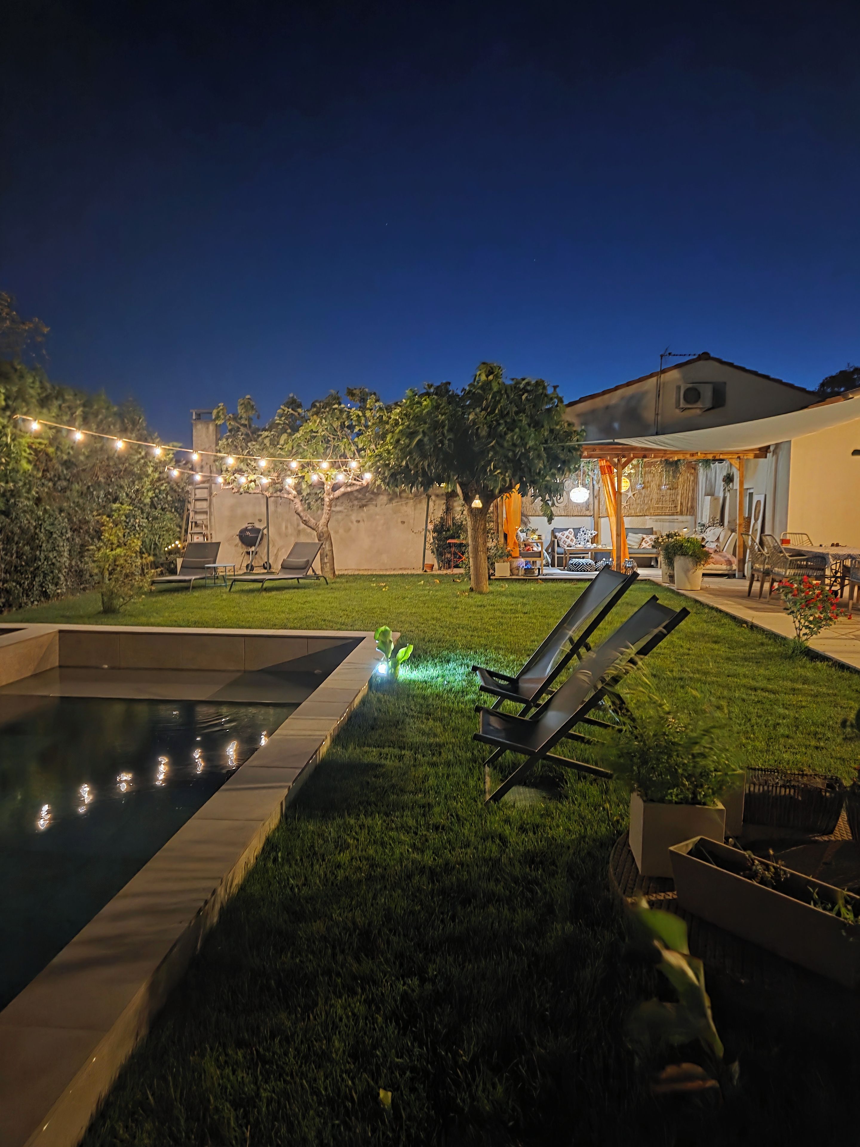 A backyard with a swimming pool, lounge chairs, and a patio area with outdoor furniture.