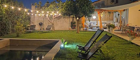 A backyard with a swimming pool, lounge chairs, and a patio area with outdoor furniture.