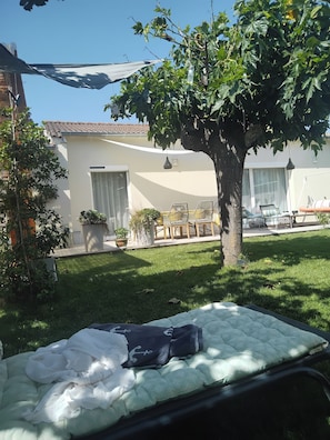 A bed with a mattress and pillows, a tree, a chair, and a table in a sunny outdoor area. - House with a private pool in the heart of Montélimar (Montélimar)