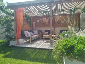 Zona relax esterna con pergola in legno, sedute imbottite e decorazioni murali.