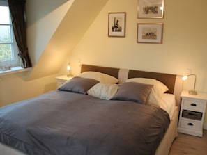 A bedroom with a bed, two bedside tables, a window with curtains, and two framed pictures on the wall. - Theodor-storm-str. 3a (Sylt)