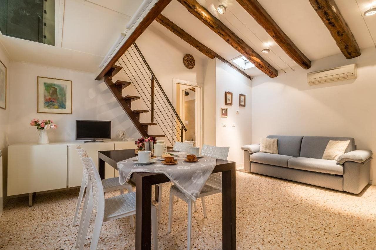 Un área de comedor con una mesa preparada para dos personas, un sofá, un televisor y una escalera.