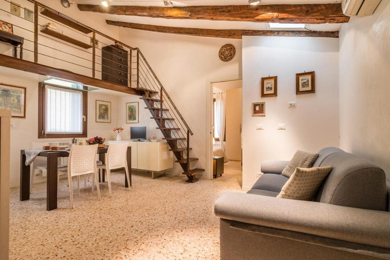 Un amplio salón con una escalera, un sofá, una mesa de comedor con sillas y obras de arte en las paredes.