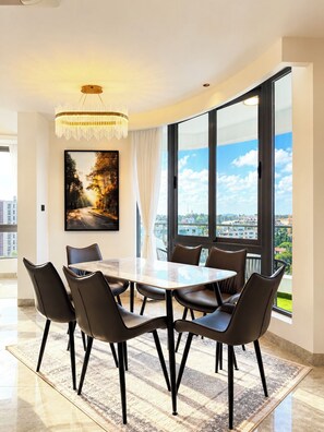 Een eetgedeelte met een tafel en stoelen, een kroonluchter, een groot raam met stadszicht en een schilderij aan de muur.