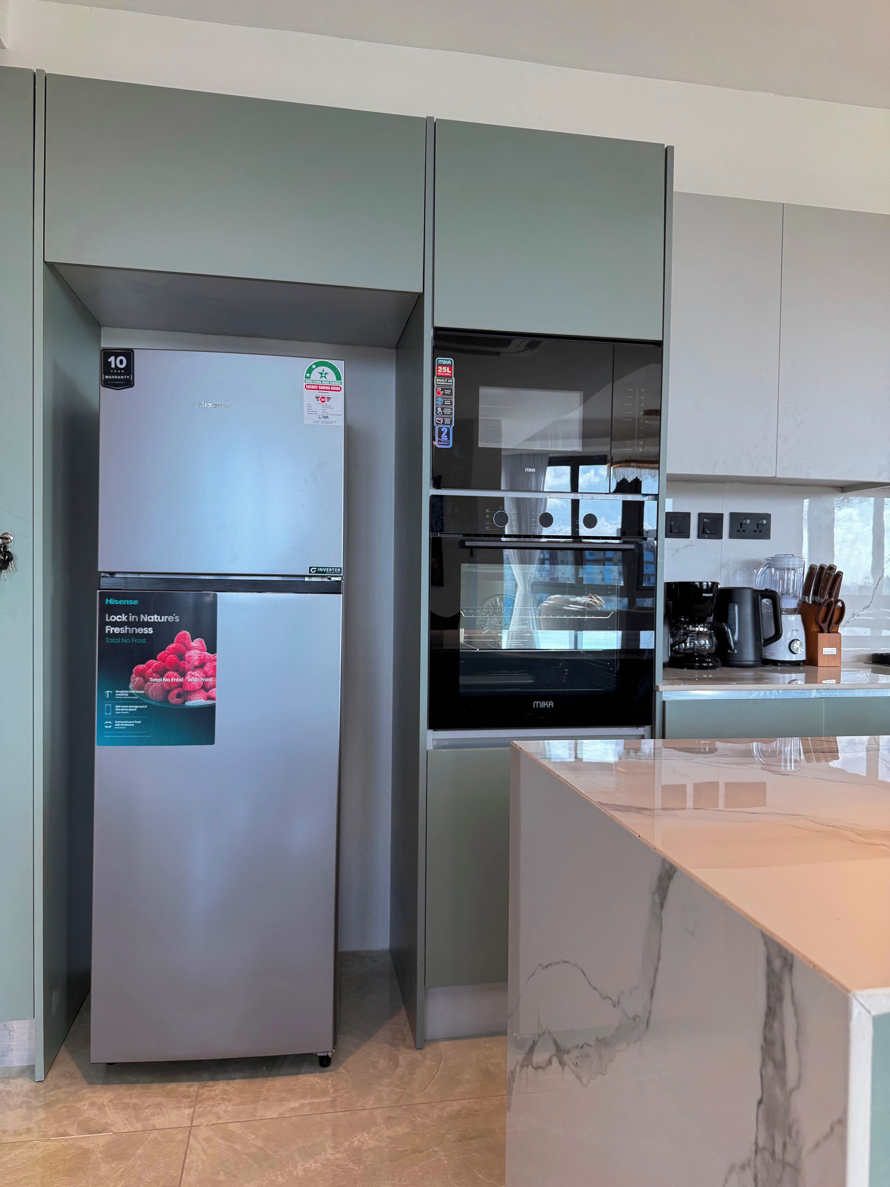 Une cuisine moderne dotée d’un réfrigérateur en acier inoxydable, d’un four encastré et d’un plan de travail en marbre.